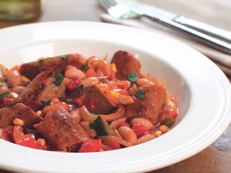 A casserole made with Quorn Sausages, beans, and sweetcorn served in a white bowl.