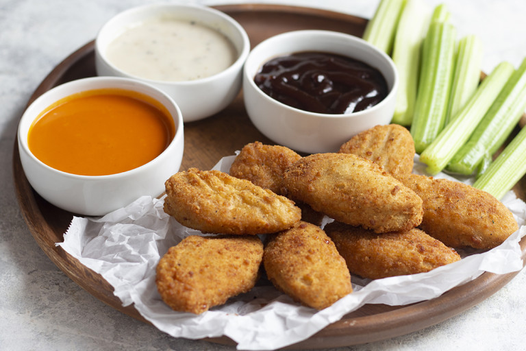 Quorn vegan Buffalo Wings with Trio of Dips on a wooden plate with celery 