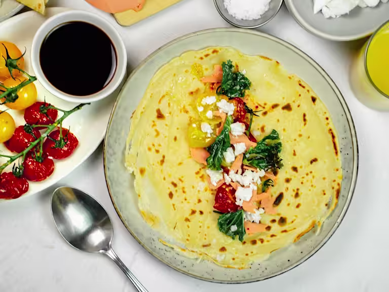 Pancakes with yellow and red cherry tomatoes on the vine next to a serving pot of balsamic vinegar.