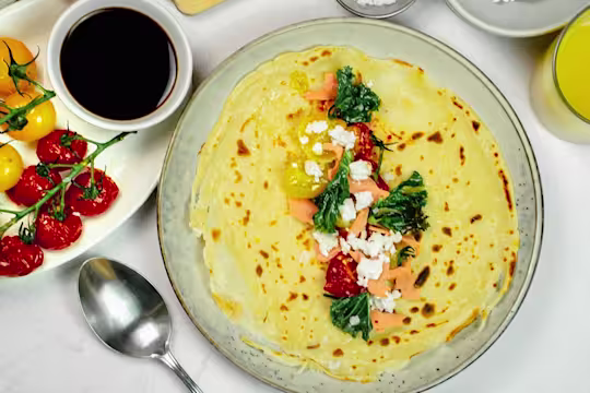 Pancakes with yellow and red cherry tomatoes on the vine next to a serving pot of balsamic vinegar.