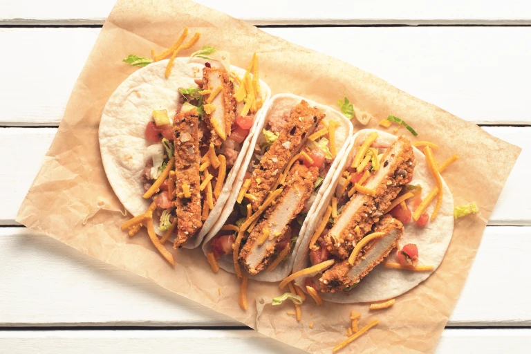 Veggie tacos made with Quorn Vegan Hot & Spicy Burgers, peppers and cheese in tortilla wraps served on baking paper