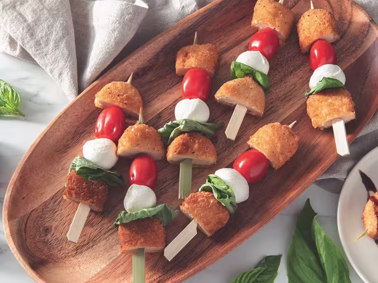 Vegetarian skewers with Quorn crispy nuggets, cherry tomatoes, mozzarella balls, and basil served on a wooden platter