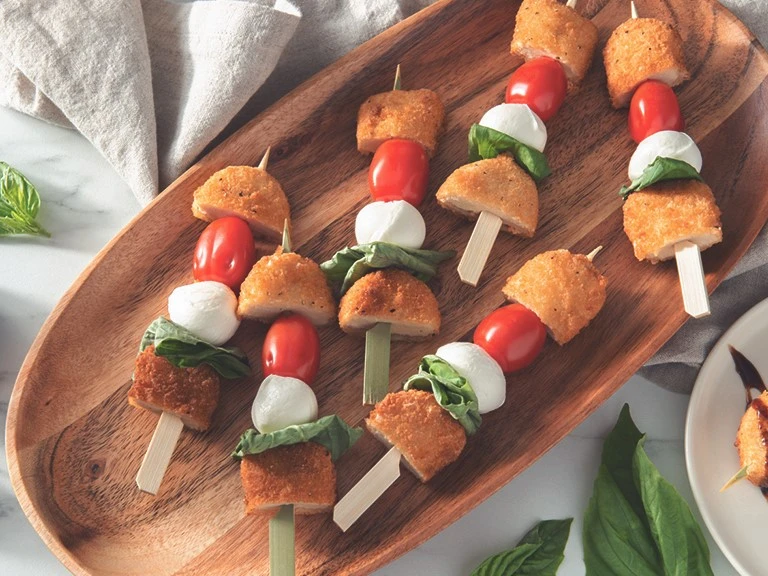 Vegetarian skewers with Quorn crispy nuggets, cherry tomatoes, mozzarella balls, and basil served on a wooden platter