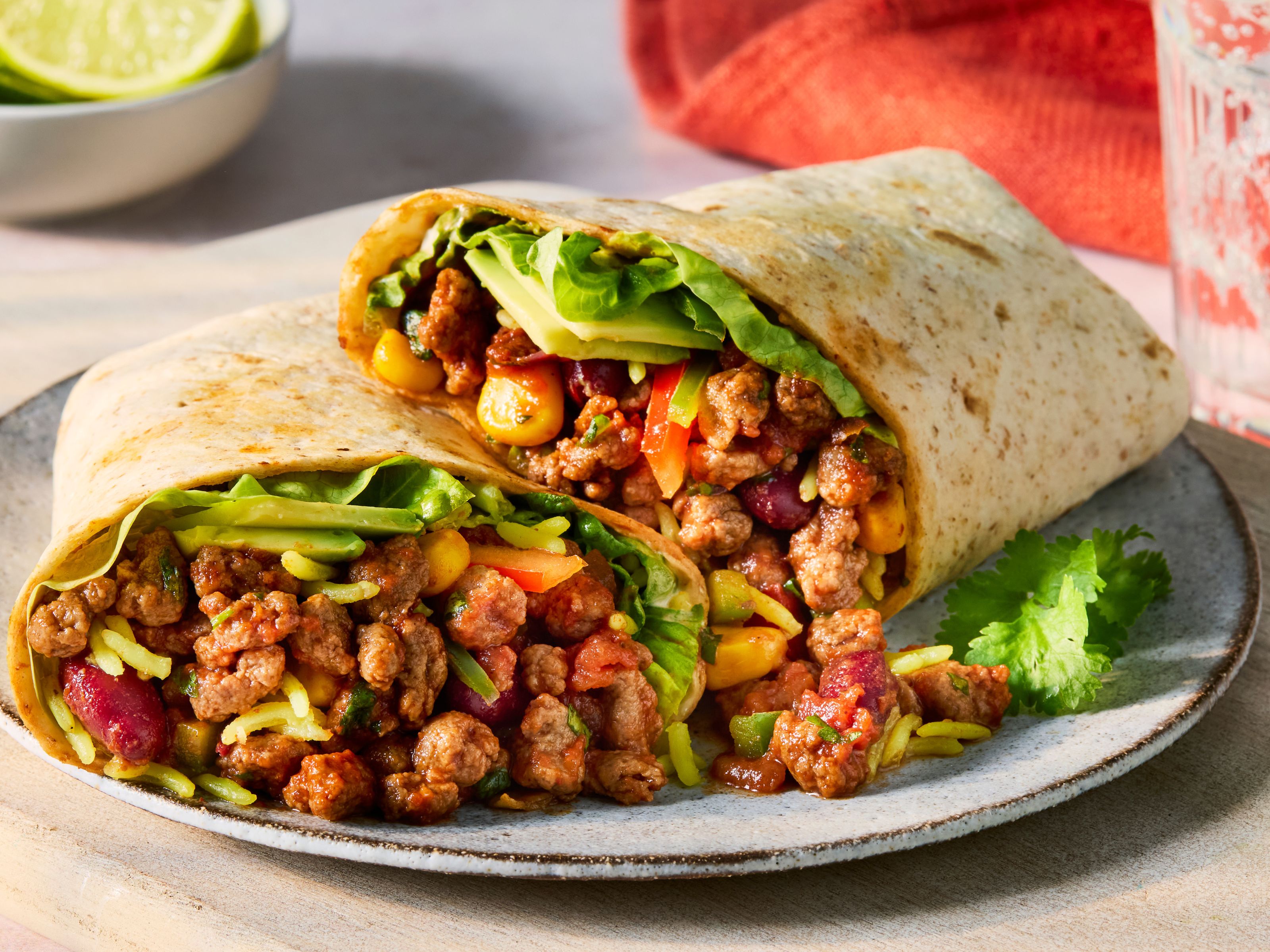 Two vegetarian burritos filled with spicy Quorn Mince and red onion, kidney beans, sweetcorn, coriander, pepper, avocado and pilau rice, on a white plate with a white background.