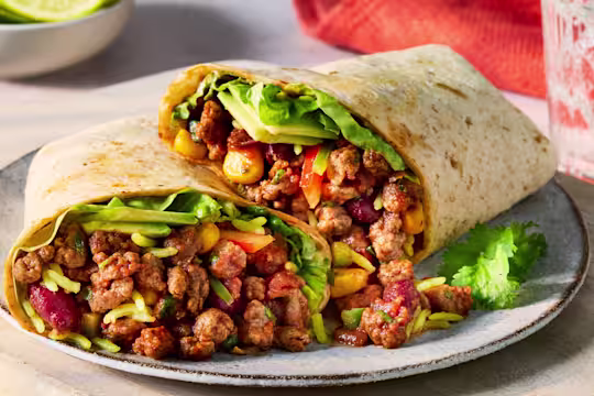 Two vegetarian burritos filled with spicy Quorn Mince and red onion, kidney beans, sweetcorn, coriander, pepper, avocado and pilau rice, on a white plate with a white background.