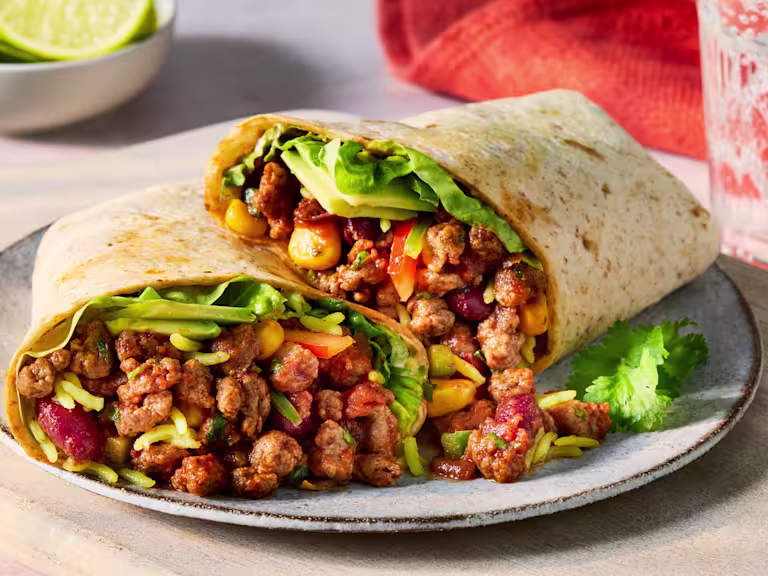 Two vegetarian burritos filled with spicy Quorn Mince and red onion, kidney beans, sweetcorn, coriander, pepper, avocado and pilau rice, on a white plate with a white background.