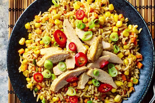 Quorn Meatless Fillets sliced served on top of a bed of vegetable rice served in a dark dish with a fork on the side.