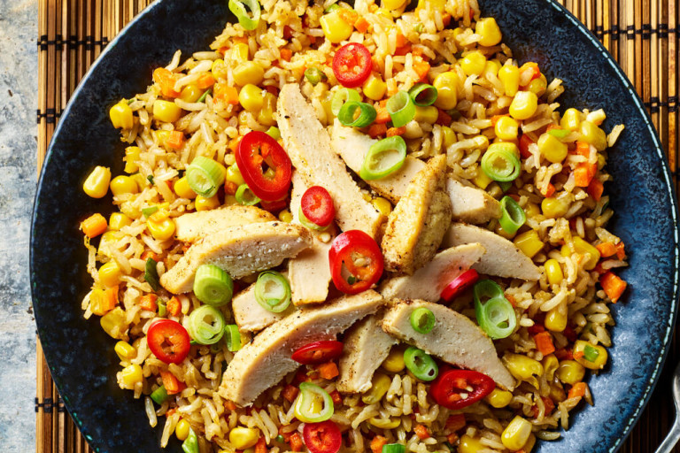 Quorn Meatless Fillets sliced served on top of a bed of vegetable rice served in a dark dish with a fork on the side. 