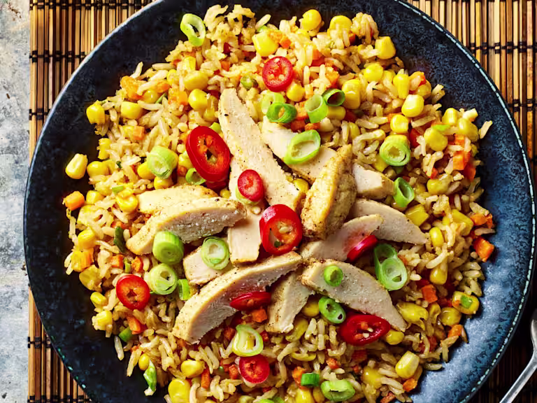 Quorn Meatless Fillets sliced served on top of a bed of vegetable rice served in a dark dish with a fork on the side.
