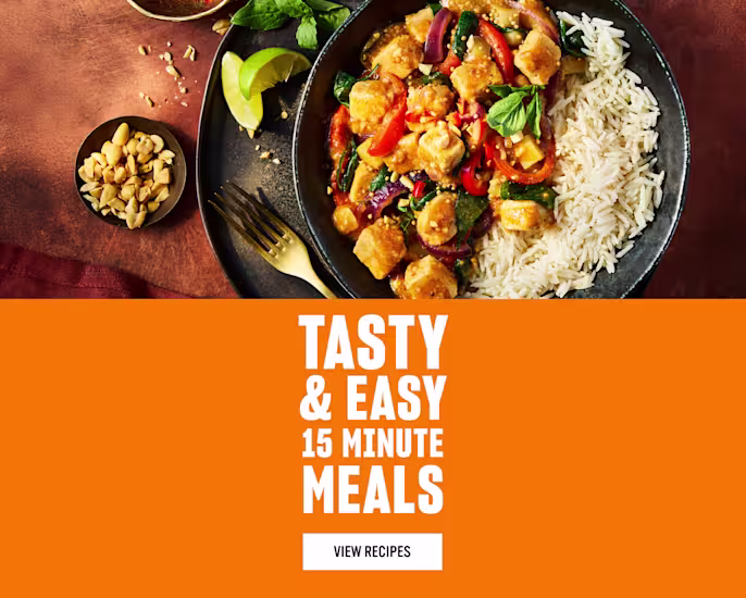 A bowl of rice served with a colourful stir-fry of tofu, red peppers, spinach, and peanuts, garnished with basil and lime wedges, next to text reading ‘Tasty & Easy 15 Minute Meals - View Recipes’ on an orange background.