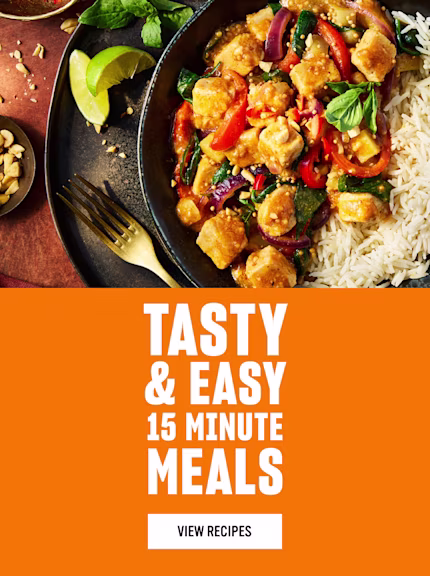 A bowl of rice served with a colourful stir-fry of tofu, red peppers, spinach, and peanuts, garnished with basil and lime wedges, next to text reading ‘Tasty & Easy 15 Minute Meals - View Recipes’ on an orange background.