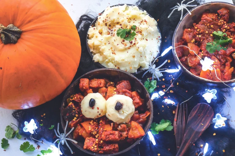 Pumpkin curry with Quorn Pieces in a bowl with balls of mash on top for eyes next to a pumpkin, bowl of mash and ghost lights