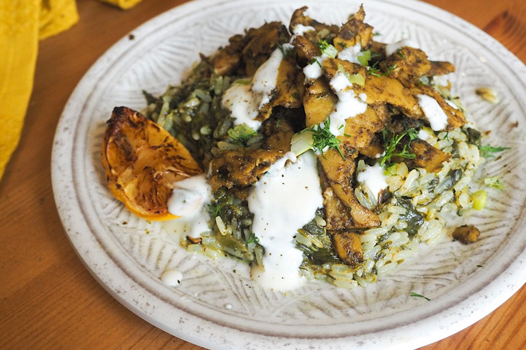 A plate of vegan Greek Spanakorizo spinach rice made with Quorn Makes Amazing Turkish-Style Strips topped with yoghurt with a charred lemon wedge on the side.