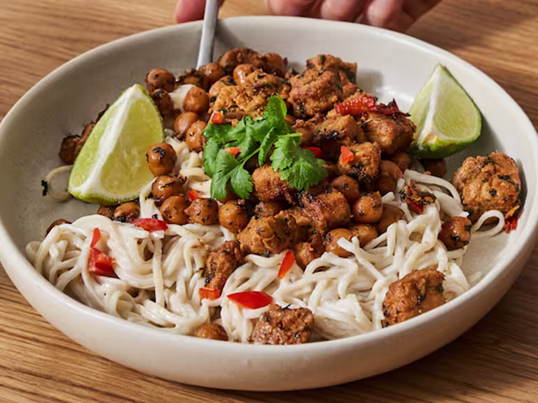 En stor skål med Quorn vegetariska asiatiska gryta med krämiga nudlar serverad i en krämfärgad skål