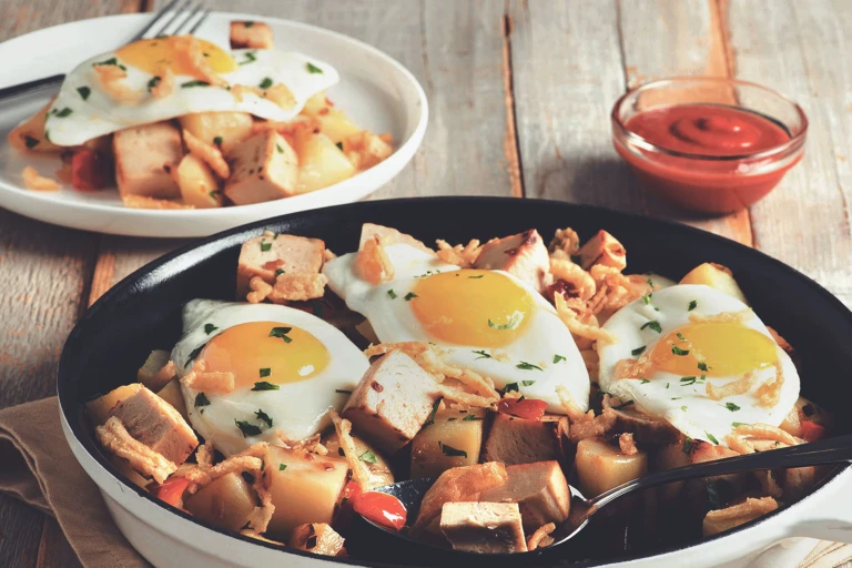 A skillet full of potatoes and cubed Quorn Meatless Roast topped with three fried eggs and crispy onions.