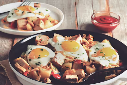 A skillet full of potatoes and cubed Quorn Meatless Roast topped with three fried eggs and crispy onions.