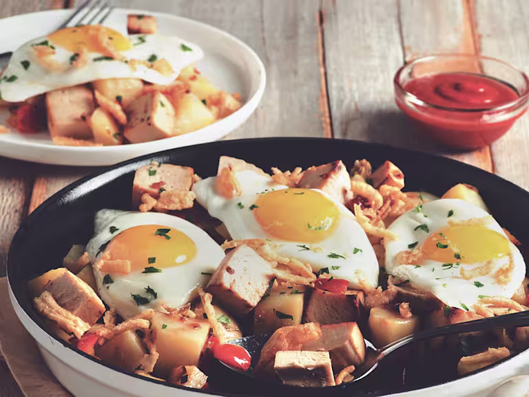 A skillet full of potatoes and cubed Quorn Meatless Roast topped with three fried eggs and crispy onions.