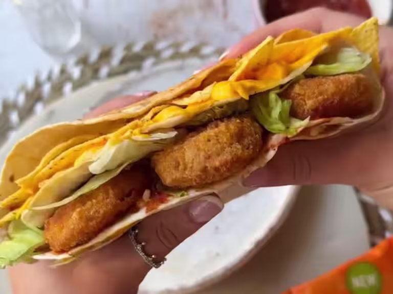 Hands holding a Quorn Cheesy Nacho Nuggs in a wrap wtih tortilla chips and salad