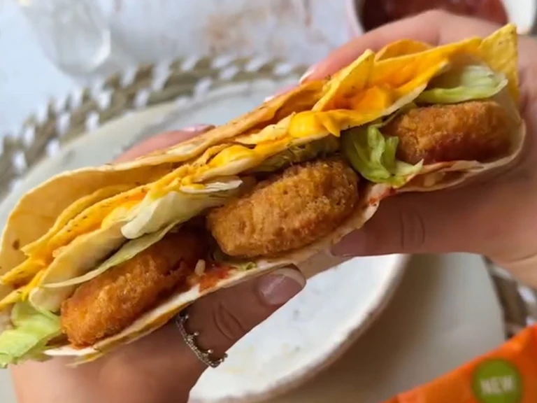 Hands holding a Quorn Cheesy Nacho Nuggs in a wrap wtih tortilla chips and salad