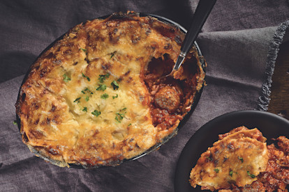 A lasagne made with Quorn Swedish Style Meatballs topped with cheese and parsley in a black baking dish.