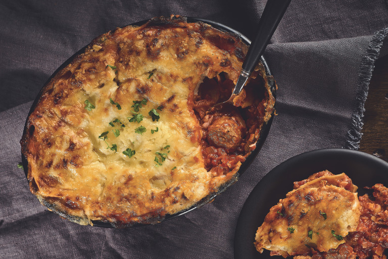 A lasagne made with Quorn Swedish Style Meatballs topped with cheese and parsley in a black baking dish.