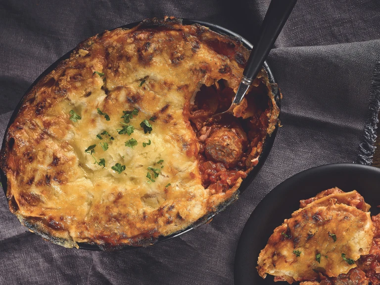 A lasagne made with Quorn Swedish Style Meatballs topped with cheese and parsley in a black baking dish.
