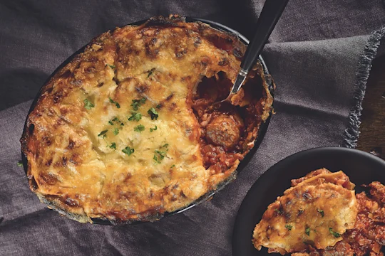 A lasagne made with Quorn Swedish Style Balls topped with cheese and parsley in a black baking dish.