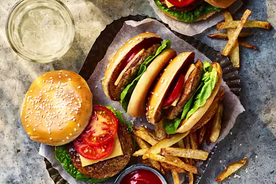 Four Quorn Classic Vegetarian Cheeseburger with one open to show the toppings served alongside fries and sauce.