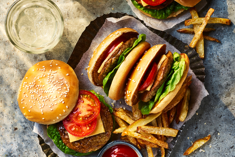Four Quorn Classic Vegetarian Cheeseburger with one open to show the toppings served alongside fries and sauce. 