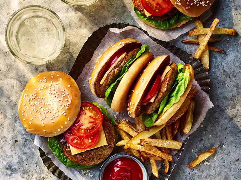 Four Quorn Classic Vegetarian Cheeseburger with one open to show the toppings served alongside fries and sauce.