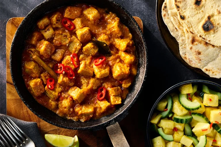 Quorn Vegetarian Rendang Curry served in a dark dish with a side of pineapple and cucumber salad and flatbread. 