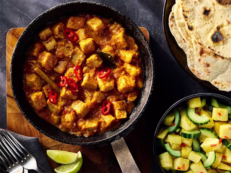 Quorn Vegetarian Rendang Curry served in a dark dish with a side of pineapple and cucumber salad and flatbread.