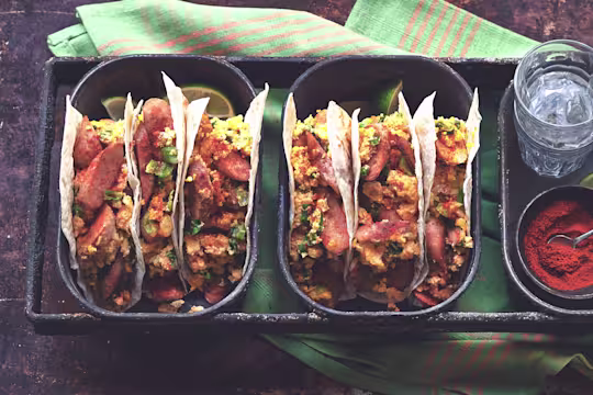 Two dishes of three flour tortilla tacos filled with Quorn Sausage, eggs, and cheese.