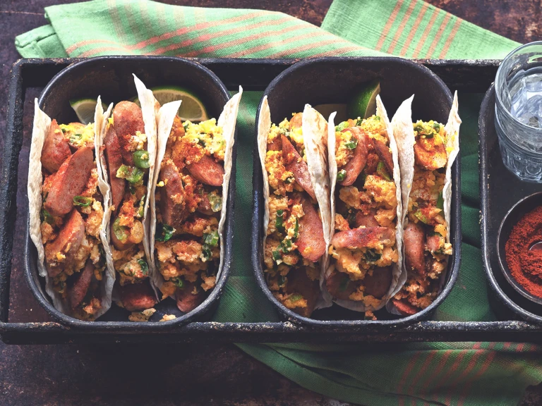 Two dishes of three flour tortilla tacos filled with Quorn Sausage, eggs, and cheese.