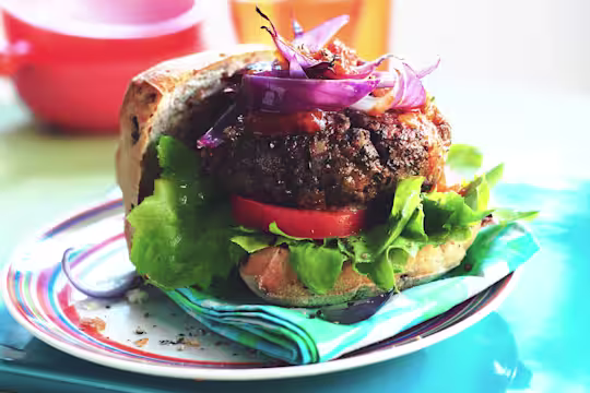 Quorn Vegetarian Mince burger in an open bun with salad, tomato and red onion on a striped plate.