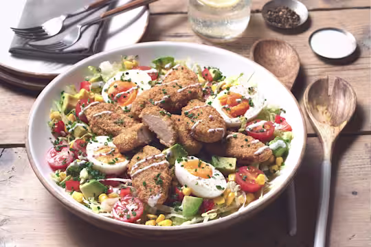 A large portion of Quorn Vegetarian Cobb Salad with Quorn Meatless ChiQin Wings on top served with cutlery on the side.