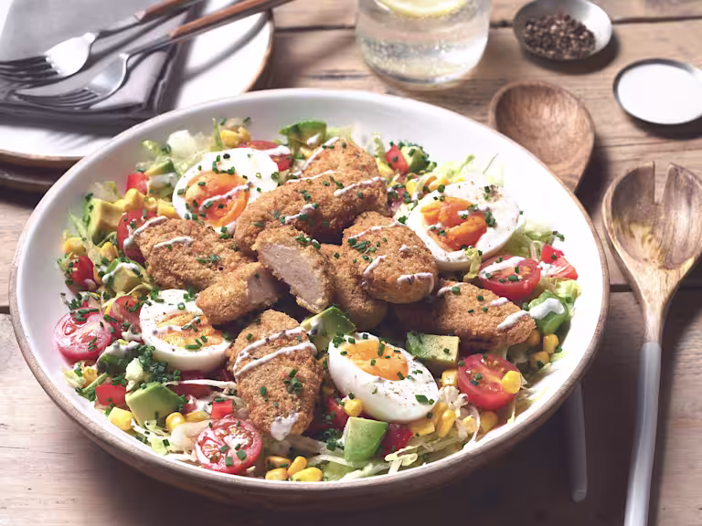 A large portion of Quorn Vegetarian Cobb Salad with Quorn Meatless ChiQin Wings on top served with cutlery on the side.