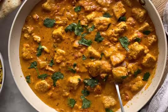 Vegetarian Quorn pieces curry in a dish garnished with coriander and served with a spoon.