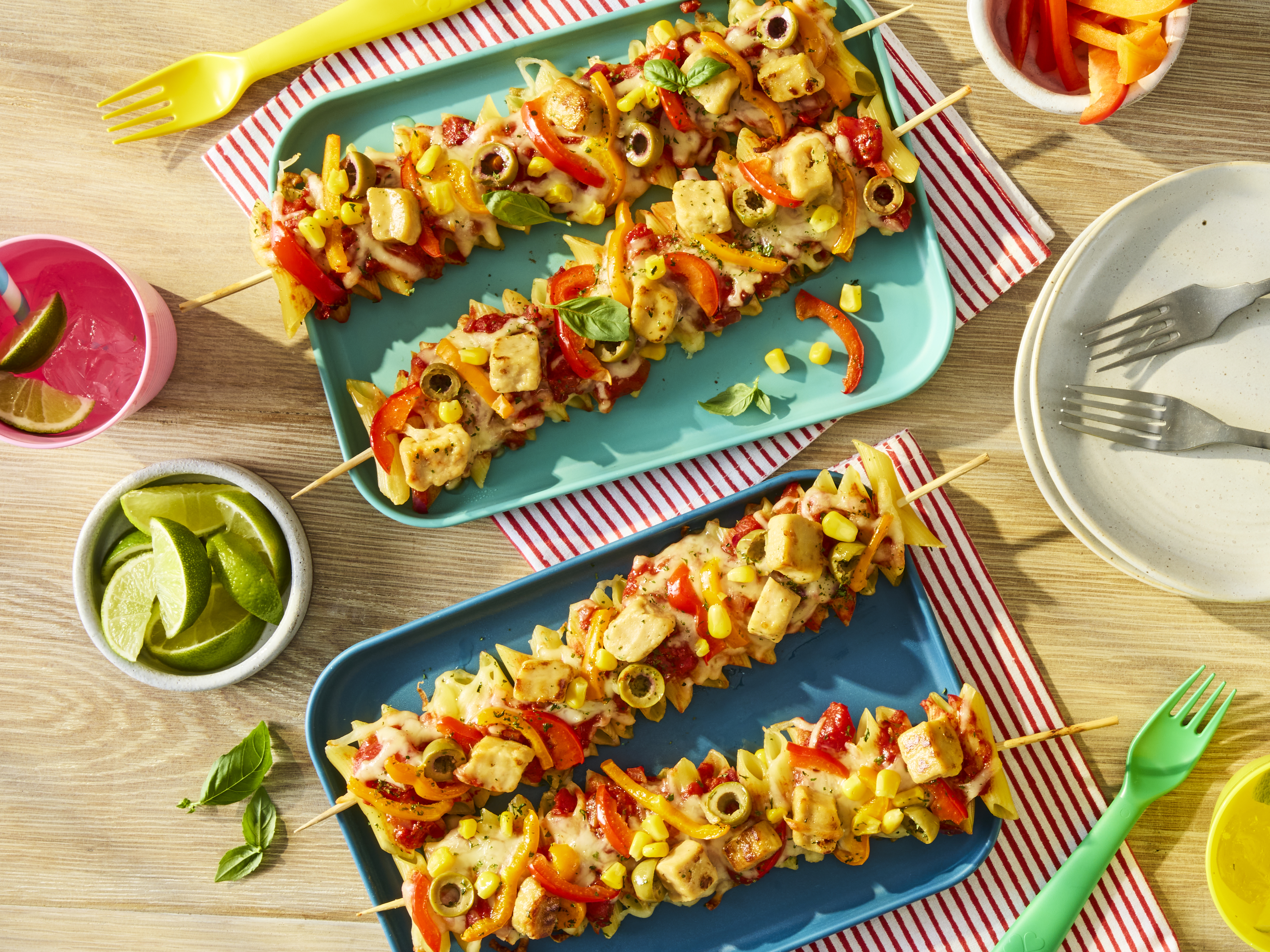Penne pasta and Quorn Pieces threaded onto skewers with sliced peppers, topped with pizza sauce, melted mozzarella and olives. Served on a plate.