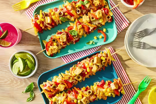 Penne pasta and Quorn Pieces threaded onto skewers with sliced peppers, topped with pizza sauce, melted mozzarella and olives. Served on a plate.