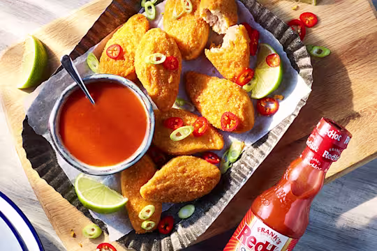 Vegan Buffalo wings topped with red and green chillies with the sauce on the side next to a bottle of Franks redhot original Cayenne Pepper Sauce.