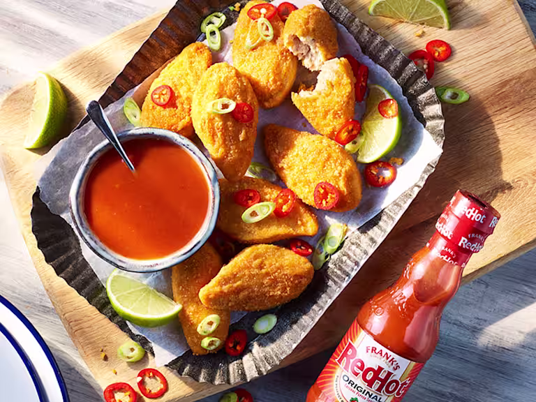 Vegan Buffalo wings topped with red and green chillies with the sauce on the side next to a bottle of Franks redhot original Cayenne Pepper Sauce.