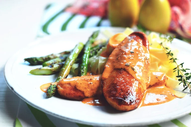 Two Quorn Fillets arranged one on top of the other topped with red pesto sauce with asparagus and pasta on the side, garnished with a spring of thyme.