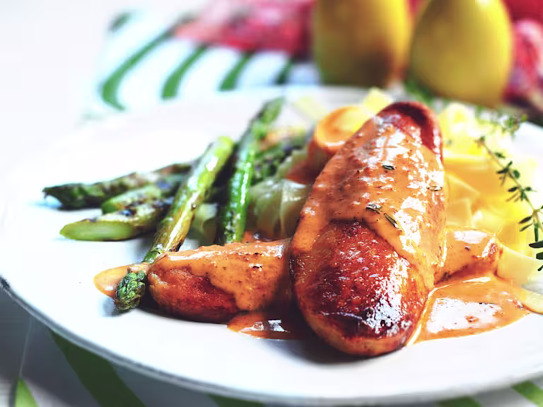 Two Quorn Fillets arranged one on top of the other topped with red pesto sauce with asparagus and pasta on the side, garnished with a spring of thyme.