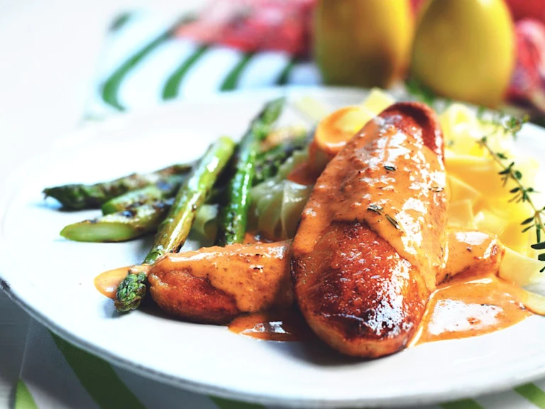 Two Quorn Fillets arranged one on top of the other topped with red pesto sauce with asparagus and pasta on the side, garnished with a spring of thyme.