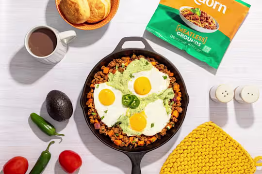 Vegetarian Breakfast Hash topped with three fried eggs with Meatless Grounds packaging on the side.