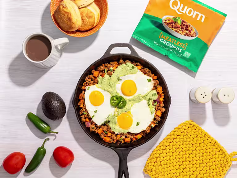 Vegetarian Breakfast Hash topped with three fried eggs with Meatless Grounds packaging on the side.