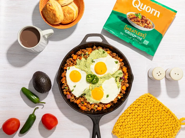 Vegetarian Breakfast Hash topped with three fried eggs with Meatless Grounds packaging on the side.