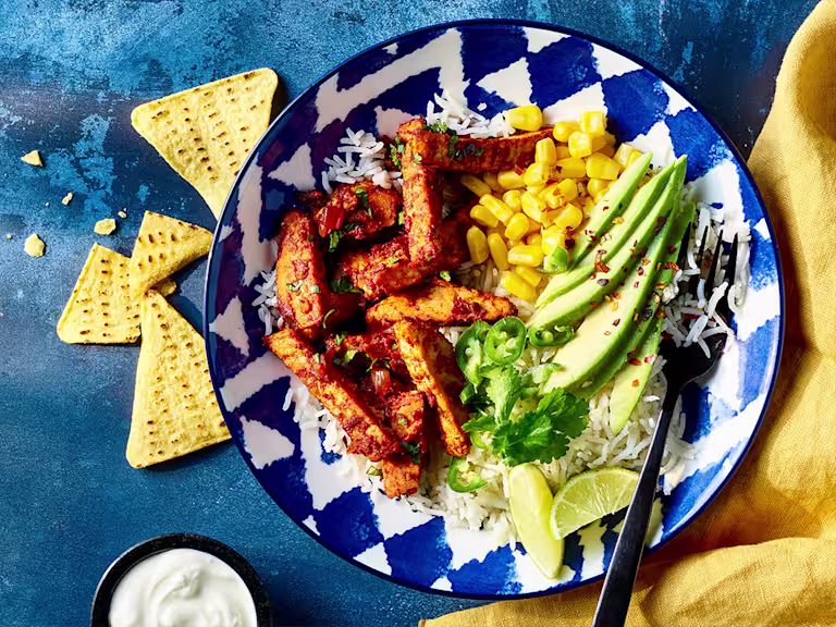 Vegetarian taco salad with Quorn sliced fillets served in a blue bowl with sour cream and nacho chips on the side.