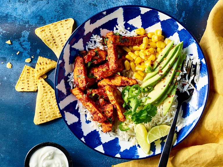 Vegetarian taco salad with Quorn roast mini fillets served in a blue bowl with sour cream and nacho chips on the side.